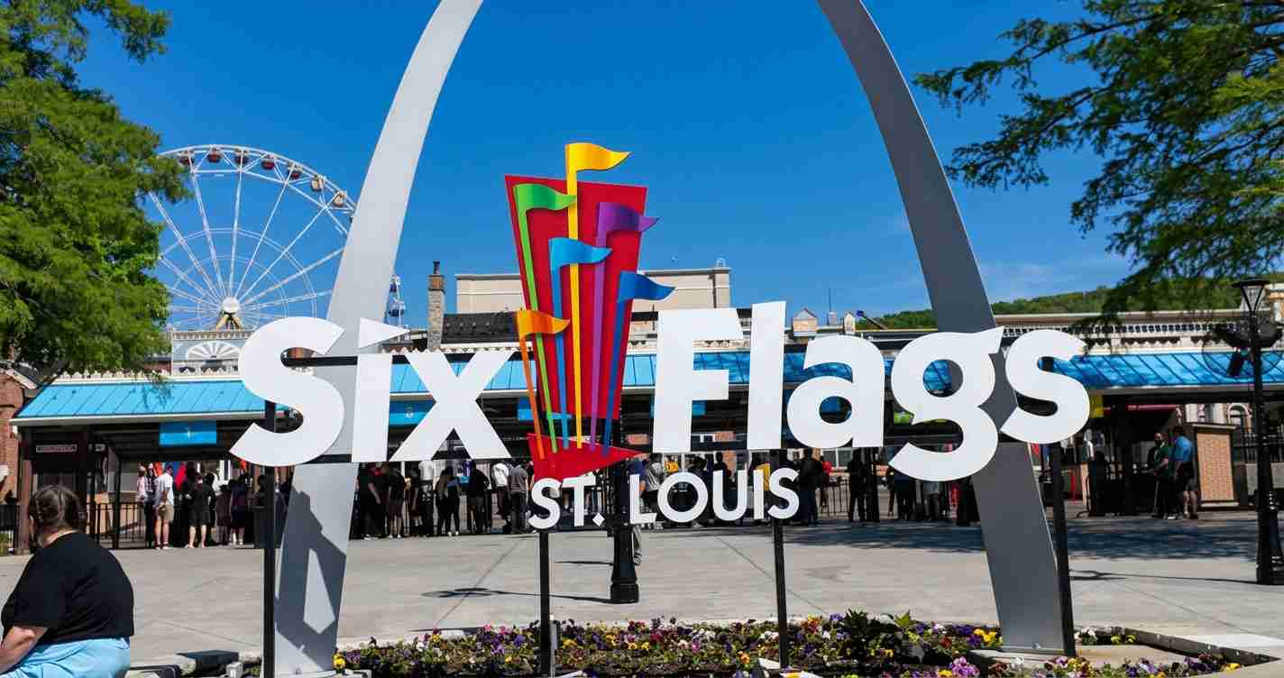 Six Flags St. Louis entrance with a large white sign, colorful vertical sculpture, and a ferris wheel in the background on a sunny day.