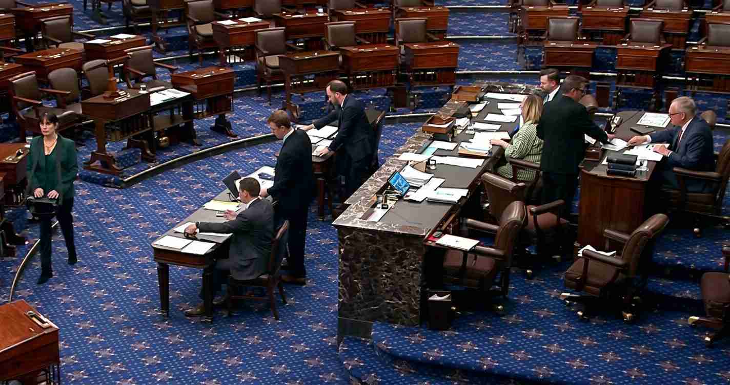 Senate chamber with lawmakers at desks around a marble podium on a blue carpeted floor with star patterns