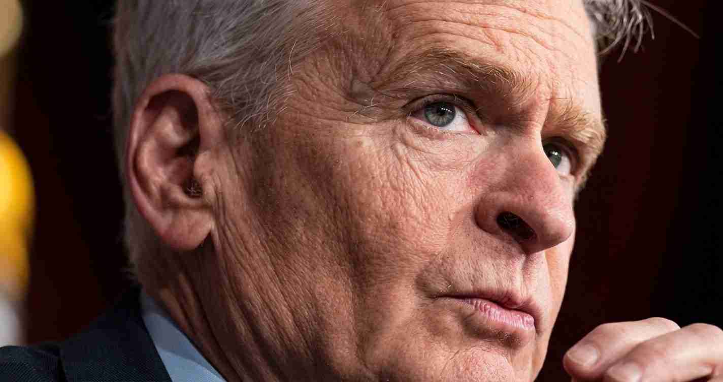 Close-up of an older man with gray hair and blue eyes, looking to the right in a thoughtful expression.