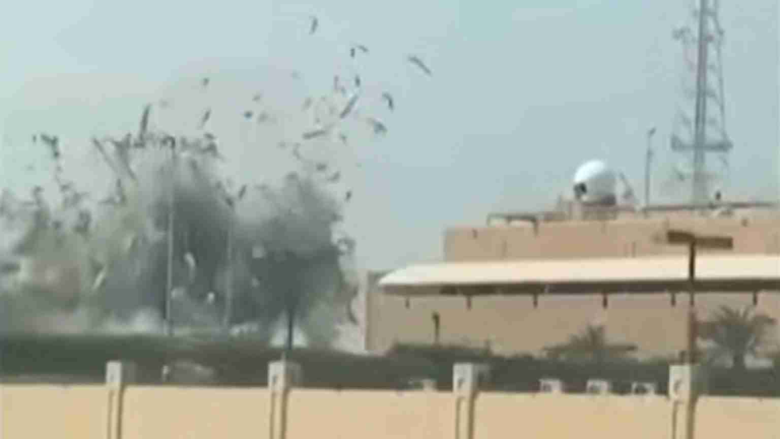 Explosion near a tan military building with a white dome, smoke and debris rising as birds scatter nearby fences and palm trees watch the scene.