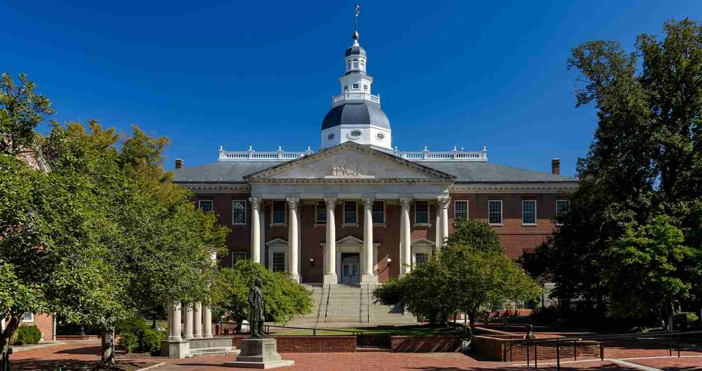 Brick university building with a domed cupola and white columns, flanked by green trees on a sunny day.