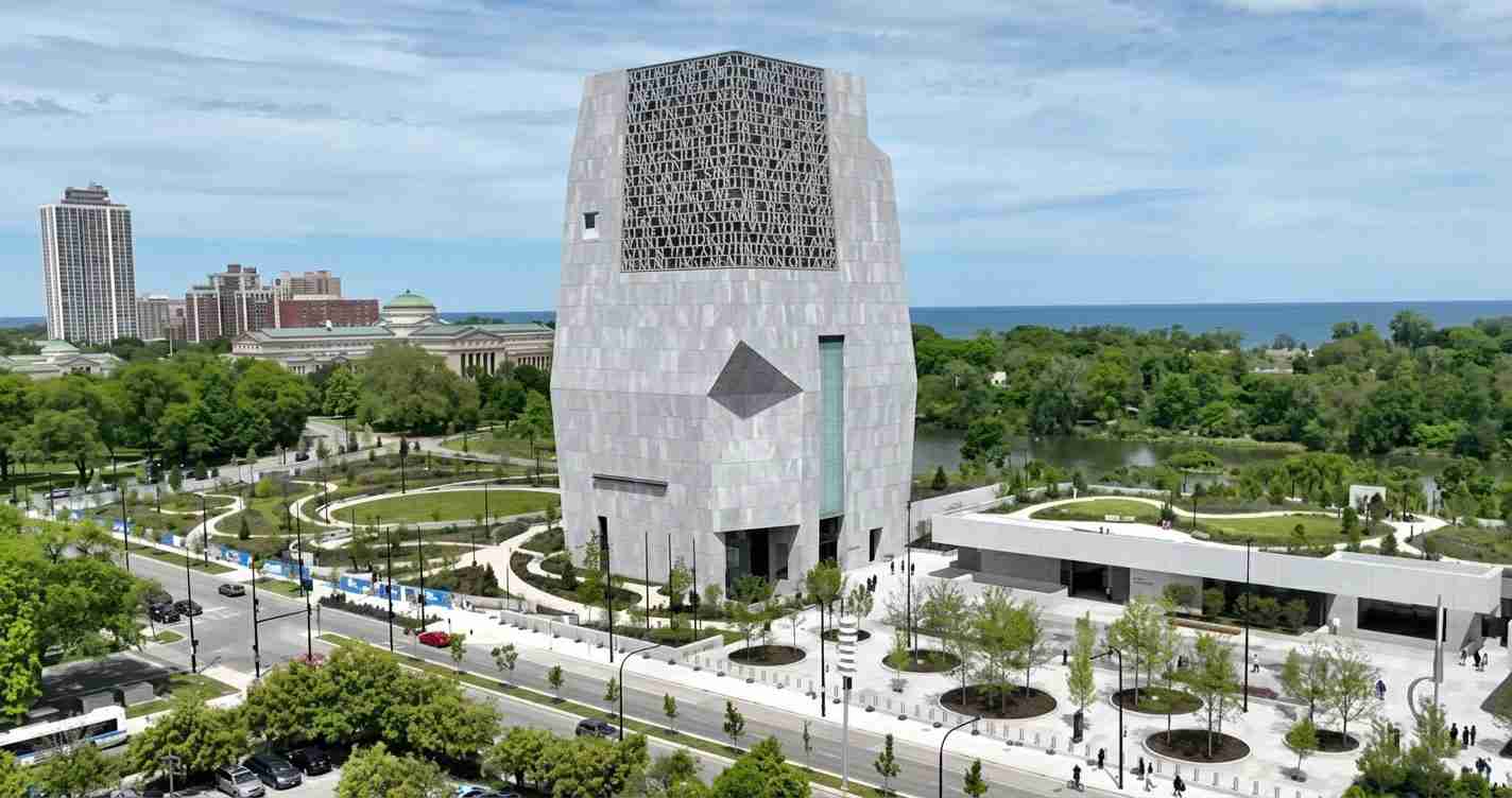 Tall sculptural tower with a perforated upper facade, set in a green park by the coast.
