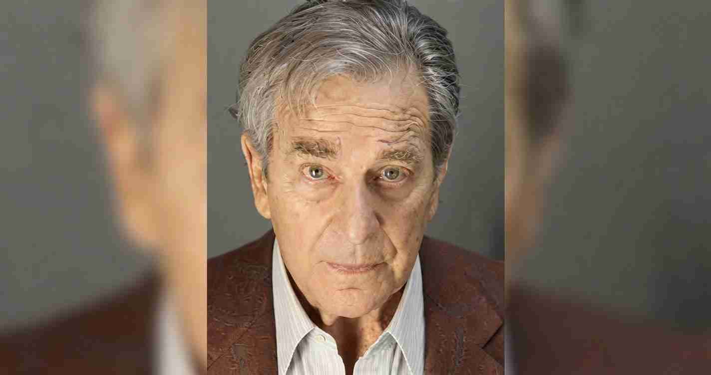 Portrait of an older man with gray hair and a serious expression, wearing a brown blazer.