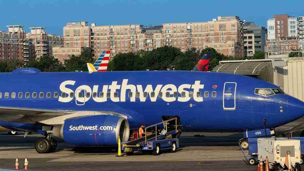 Southwest airplane parked at a gate with jet bridge and ground crew nearby.