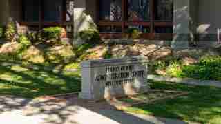 Stone pedestal sign reading 'County of Yolo Administration Center, 625 Court Street' in front of a brick-faced building with landscaping and shadows.
